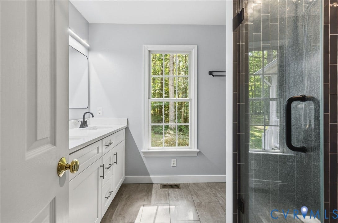 4350 Steger Creek Drive, Powhatan, VA 23139 Bathroom featuring a double-sink vanity with white cabinetry and solid-surface countertop, walk-in shower with dark tile surround and glass door, and wood-finish tile flooring