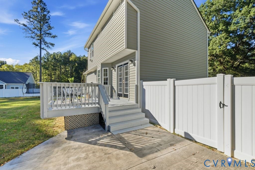 8477 Cheraw Road, Mechanicsville, VA 23116 Exterior featuring neutral-toned siding, a raised wooden deck with railings, concrete patio space, and a white privacy fence