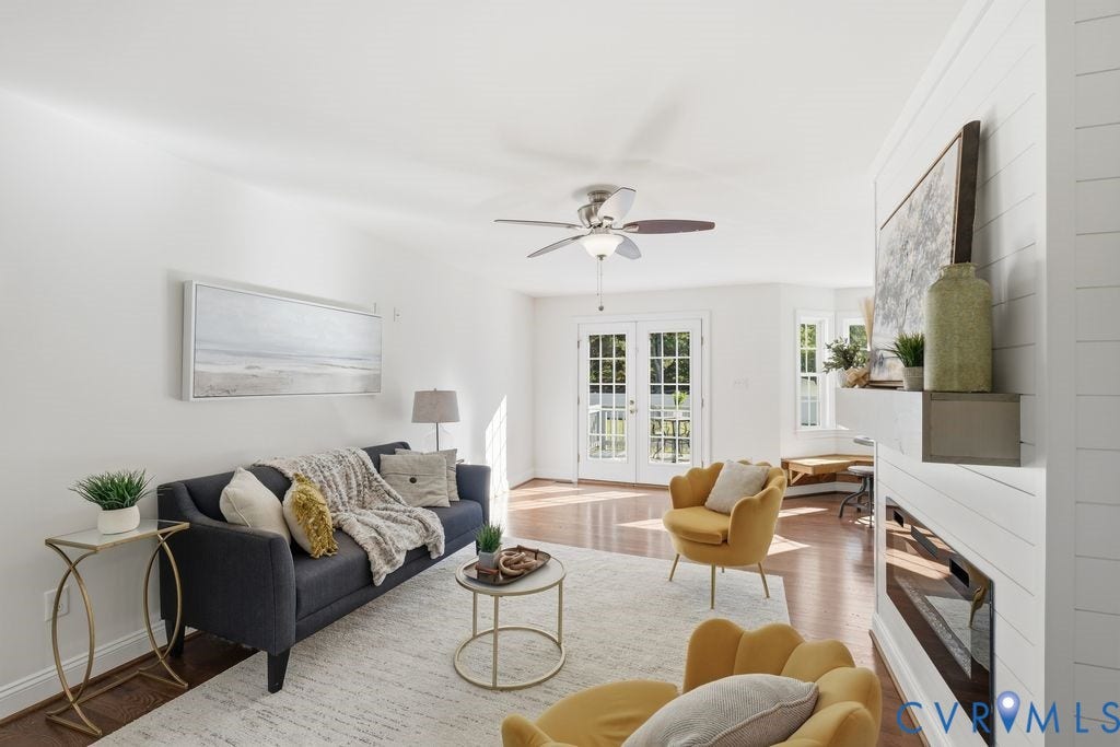 8477 Cheraw Road, Mechanicsville, VA 23116 Living area featuring a horizontal fireplace with a custom mantel, wood-finish flooring, a ceiling fan, a multi-pane glass-paneled exterior door, and a bay window