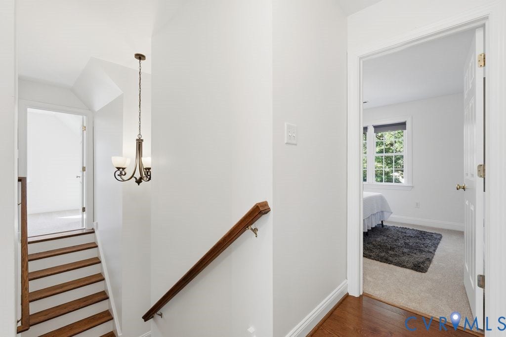 8477 Cheraw Road, Mechanicsville, VA 23116 Hallway featuring wood-finish flooring, a metal multi-light chandelier, and a wood-finish handrail
