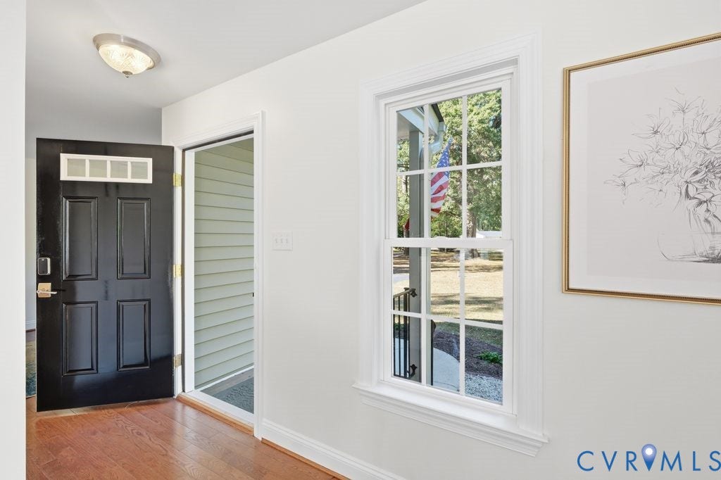 8477 Cheraw Road, Mechanicsville, VA 23116 Interior hallway featuring wood-finish flooring, a black paneled door with multi-pane transom lites, extensive white trim, a multi-pane double-hung window, and a flush-mount ceiling light fixture