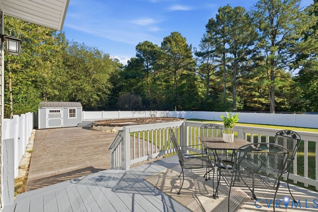 8477 Cheraw Road, Mechanicsville, VA 23116 Elevated wood deck featuring a railing system, expansive fenced backyard, detached storage building, and an above-ground pool