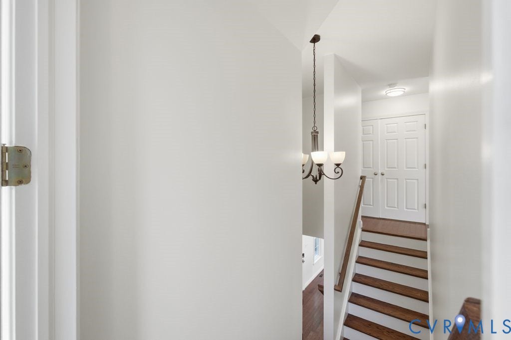 8477 Cheraw Road, Mechanicsville, VA 23116 Staircase featuring wood-finish treads, painted risers, and a metal handrail, illuminated by a multi-light chandelier and a flush-mount ceiling light, with double-panel doors