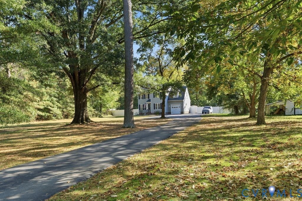 8477 Cheraw Road, Mechanicsville, VA 23116 Two-story residence featuring a paved driveway, attached garage, and white privacy fencing set within a lot with mature trees