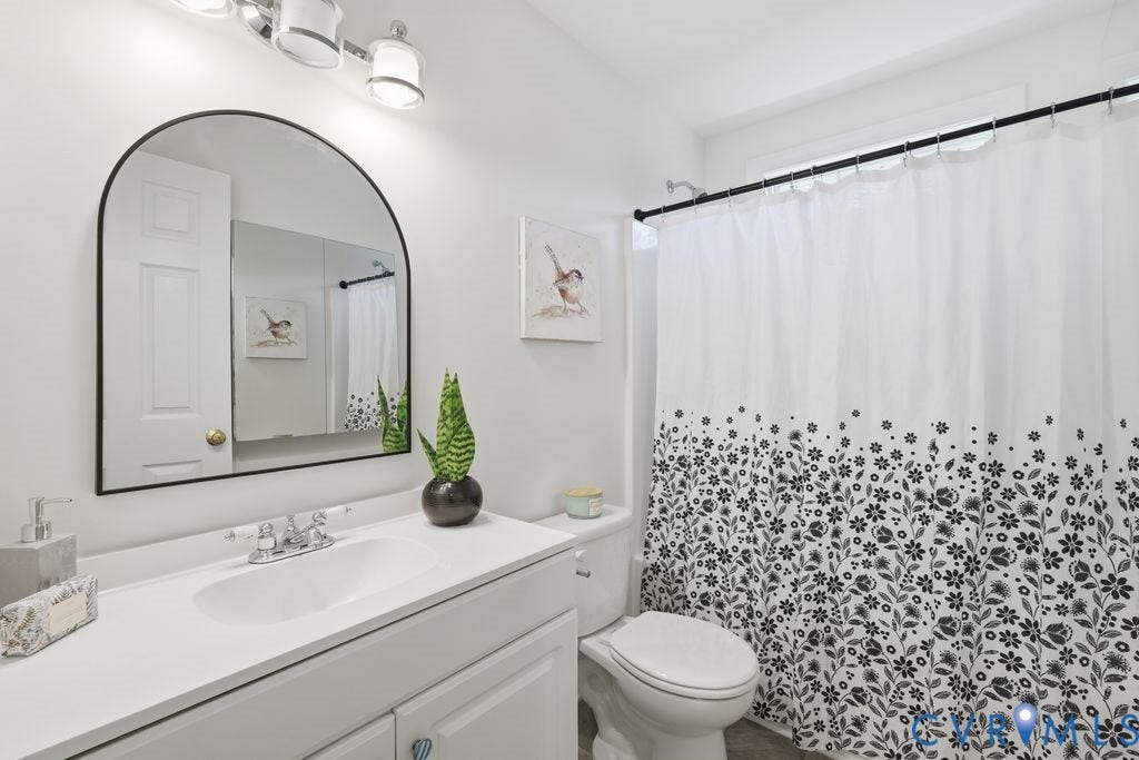 8477 Cheraw Road, Mechanicsville, VA 23116 Bathroom featuring a white vanity with a solid-surface countertop, an arched-top mirror, and a three-light wall-mounted fixture