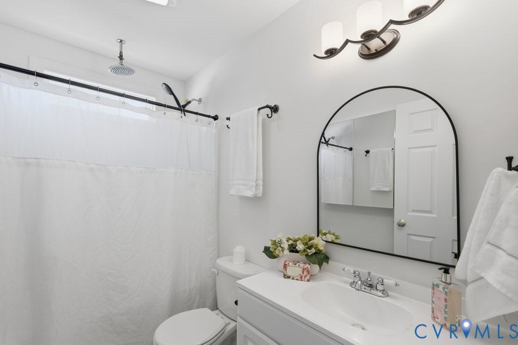 8477 Cheraw Road, Mechanicsville, VA 23116 Bathroom featuring a vanity with a countertop basin, arched wall-mounted mirror, rain shower head, three-light fixture, and matte black hardware