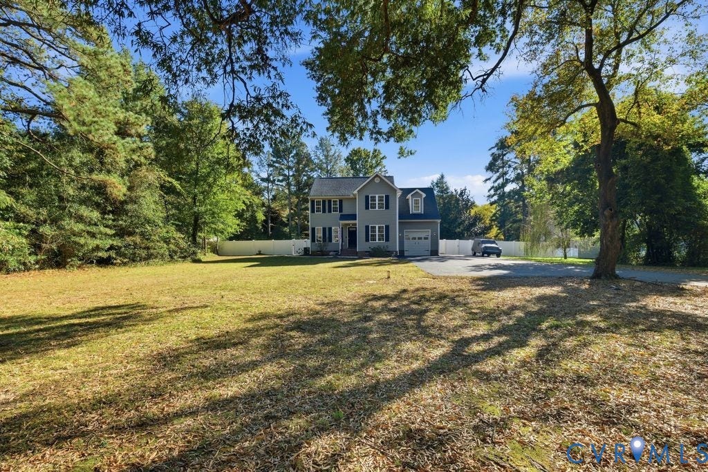 8477 Cheraw Road, Mechanicsville, VA 23116 Two-story residence featuring light-toned siding, dark window shutters, an attached garage, a paved driveway, and a white privacy fence