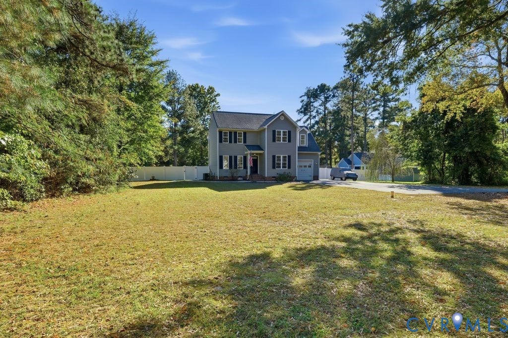 8477 Cheraw Road, Mechanicsville, VA 23116 Two-story residence featuring a gray siding exterior, attached one-car garage, white vinyl fencing, and an expansive lawn with mature trees