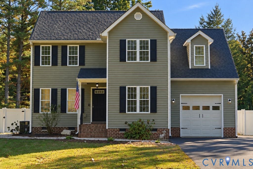 8477 Cheraw Road, Mechanicsville, VA 23116 Two-story residence featuring sage green siding, contrasting dark shutters, a brick foundation facade, an attached garage with window inserts, and a gable roofline