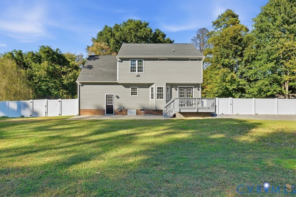 8477 Cheraw Road, Mechanicsville, VA 23116 Two-story exterior featuring light gray vinyl siding, a brick water table, a raised wood deck, a rear concrete patio, and a fully fenced perimeter