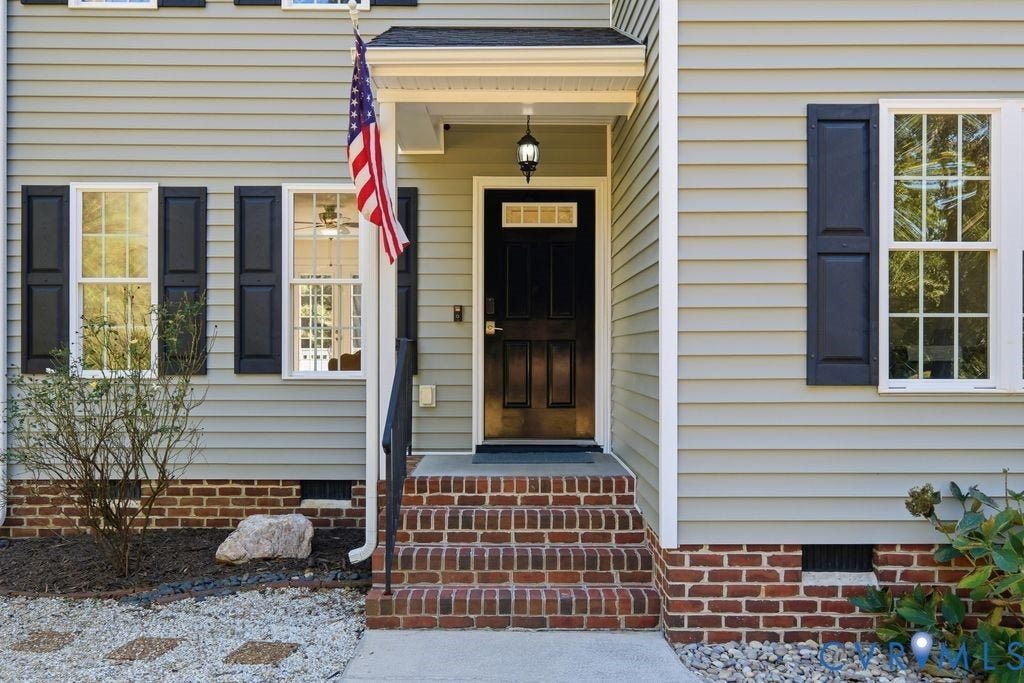 8477 Cheraw Road, Mechanicsville, VA 23116 Traditional exterior featuring horizontal siding, dark shutters, a covered entryway with an attached exterior light fixture, multi-pane windows, and brick steps leading to a dark paneled front door