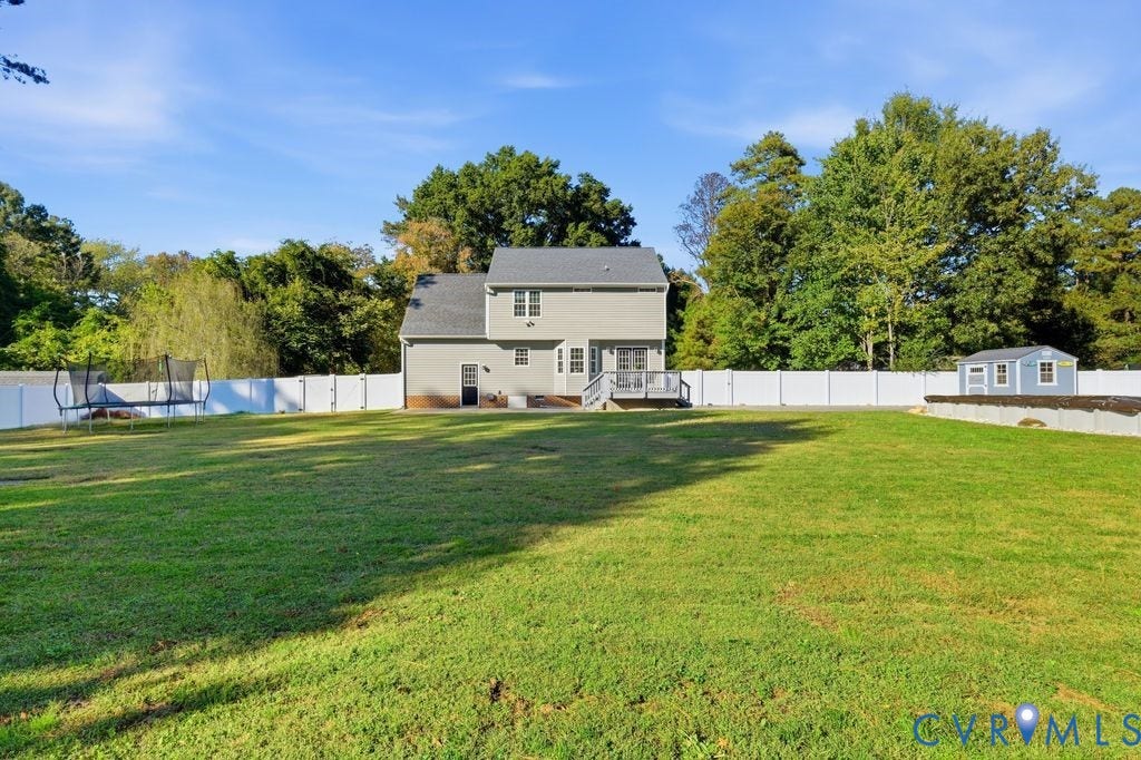 8477 Cheraw Road, Mechanicsville, VA 23116 Expansive backyard featuring a large grass lawn, white vinyl fencing, a raised wooden deck, and a detached storage structure