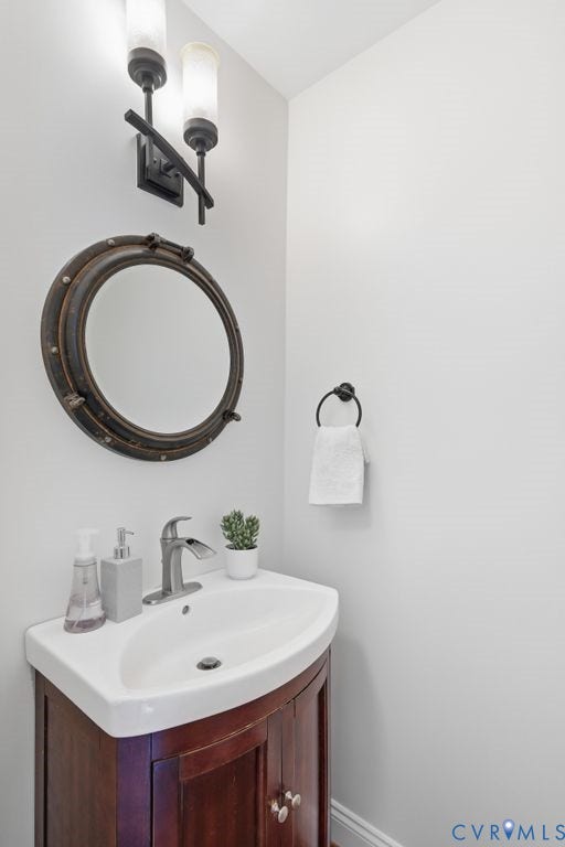 8477 Cheraw Road, Mechanicsville, VA 23116 Wood-finish pedestal vanity with a white basin, metallic faucet, circular porthole-style wall mirror, and dual-light sconce