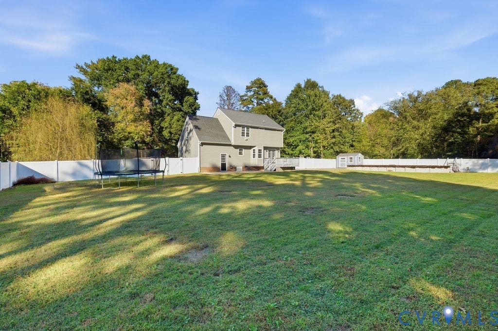 8477 Cheraw Road, Mechanicsville, VA 23116 Expansive backyard featuring a large grass lawn, white vinyl fencing, and a detached storage shed
