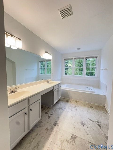 9504 Hungary Woods Drive, Glen Allen, VA 23060 Dual-sink vanity with neutral cabinetry, expansive wall-to-wall mirror, tiled soaking tub, and patterned stone-finish flooring