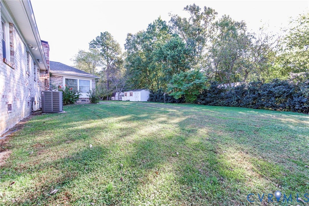 4511 Inca Drive, Ampthill, VA 23237 Expansive backyard featuring a brick exterior facade, mature trees, dense hedge landscaping, and a detached storage shed