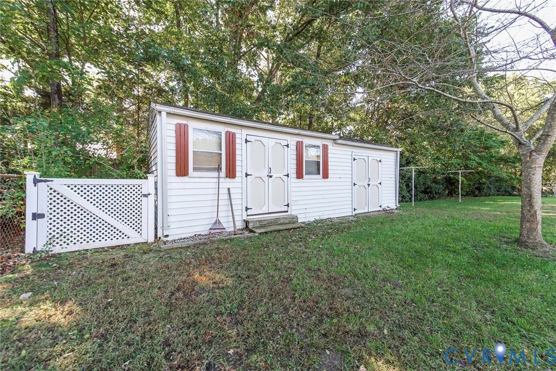 4511 Inca Drive, Ampthill, VA 23237 Storage structure featuring white horizontal siding, dual entrance doors, and decorative shutters, complemented by a white lattice fence