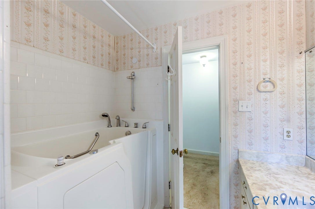 4511 Inca Drive, Ampthill, VA 23237 Step-in bathtub with integrated grab bars, white subway tile surround, laminate countertop, and wallpapered walls
