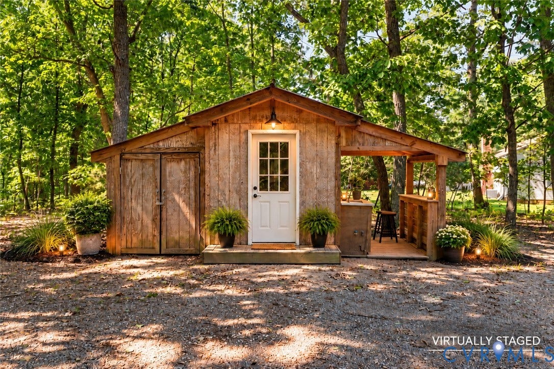2137 Scarlet Mill Lane, Powhatan, VA 23139 Rustic wood-sided outbuilding featuring a covered porch, built-in wooden bar, double-door storage access, and exterior wall-mounted lighting