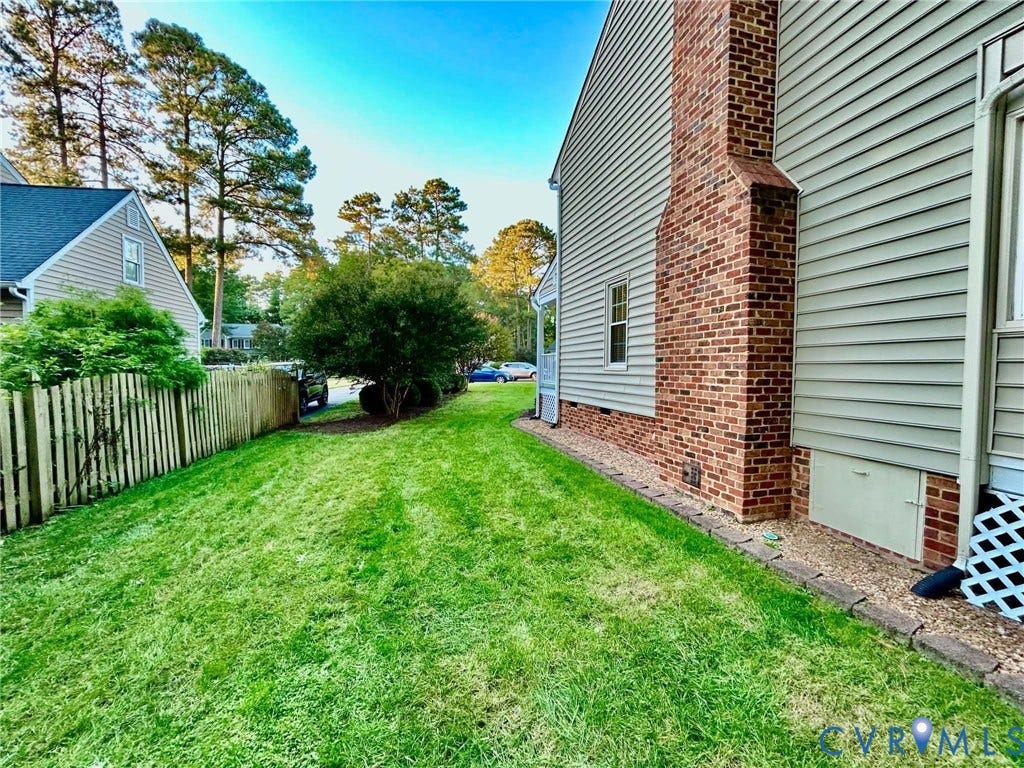 2255 Oak Bay Lane, Henrico, VA 23233 Exterior side yard featuring horizontal vinyl siding, a red brick chimney, a wood-slat privacy fence, and a stone-paver landscape border
