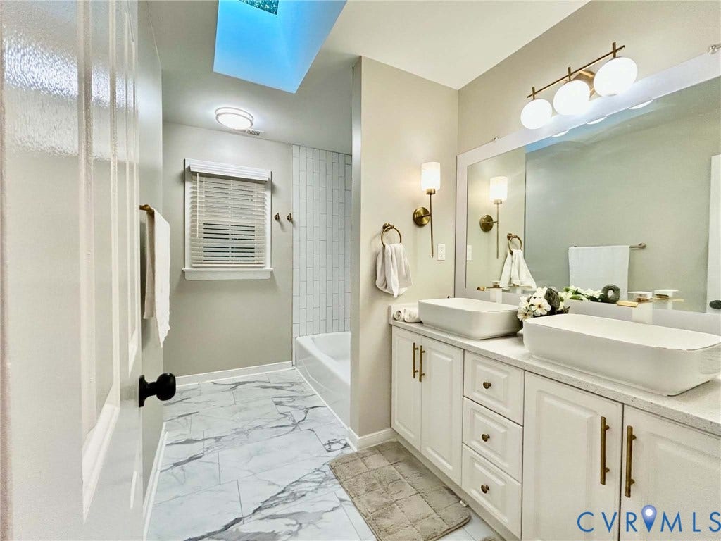 2255 Oak Bay Lane, Henrico, VA 23233 Double vanity with rectangular vessel sinks and quartz countertop, skylight, white cabinetry with brass-finish hardware, and tiled tub surround