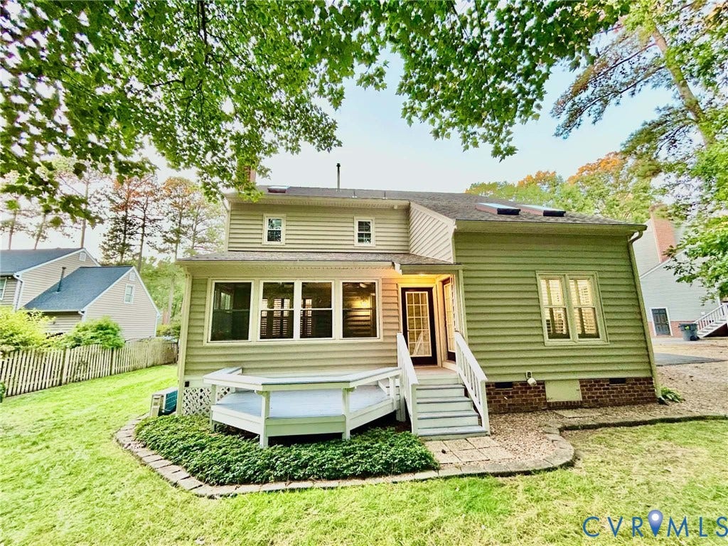 2255 Oak Bay Lane, Henrico, VA 23233 Rear exterior featuring light-colored horizontal siding, a raised white deck, brick foundation accents, roof-integrated skylights, and a stone-bordered garden bed