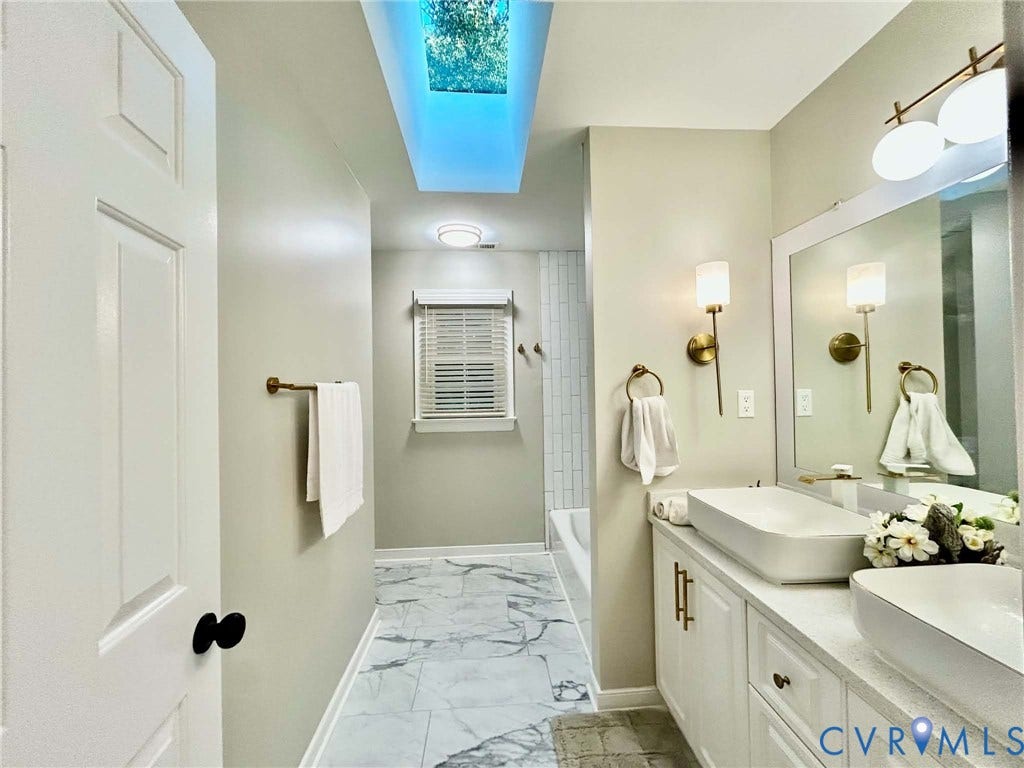 2255 Oak Bay Lane, Henrico, VA 23233 Bathroom featuring a skylight, dual vessel sinks on a quartz vanity, patterned tile flooring, and metallic wall sconces