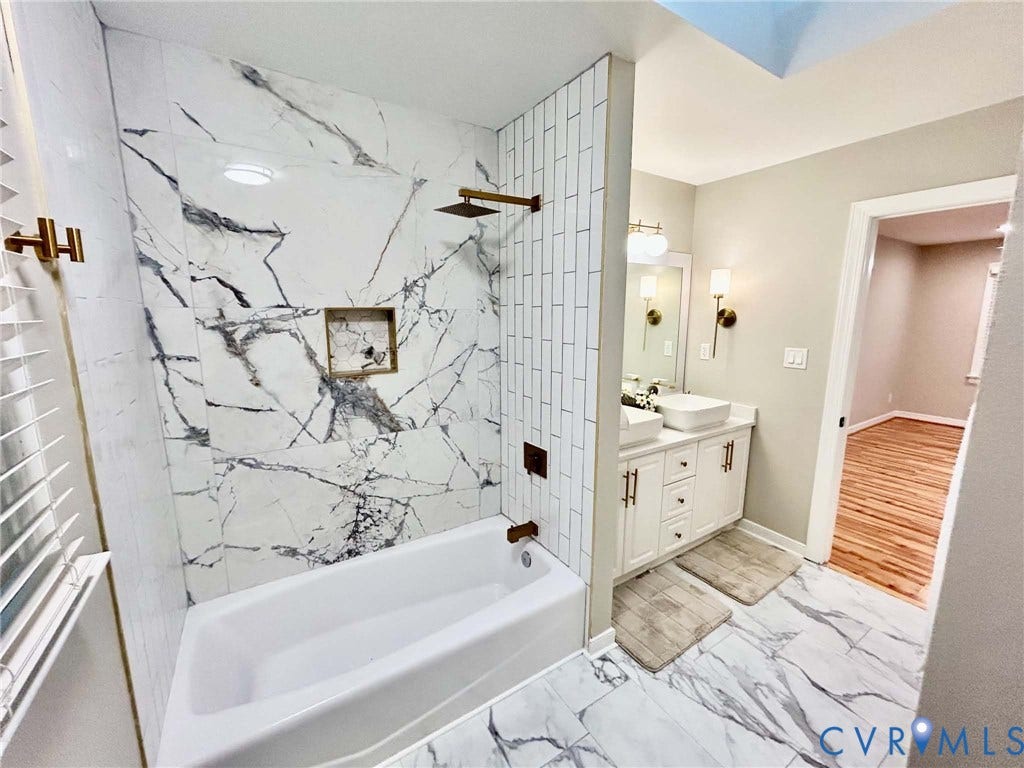 2255 Oak Bay Lane, Henrico, VA 23233 Bathroom featuring a tub-shower combination with floor-to-ceiling large-format veined tile, contrasting vertical subway tile surround, built-in recessed niche, and metallic bronze-tone fixtures, complemented by a white dual-sink vanity and matching veined floor tile