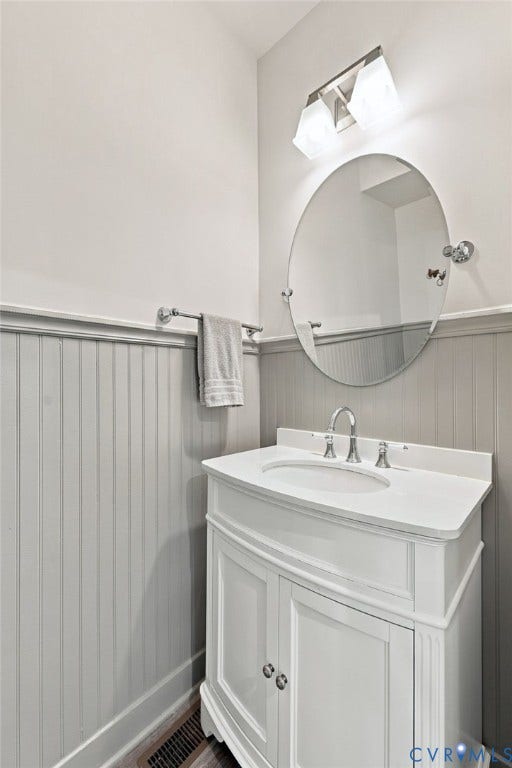1716 German School Road, Westlake Heights, Richmond, VA 23225 White vanity with integrated basin and polished chrome faucet, oval wall-mounted mirror, two-light fixture, and vertical beadboard wainscoting