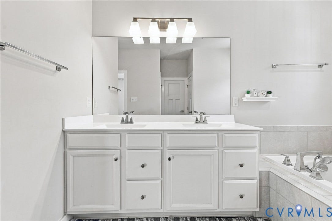1716 German School Road, Westlake Heights, Richmond, VA 23225 Double vanity with a solid-surface countertop, dual integrated sinks, polished chrome fixtures, and a large wall-mounted vanity mirror featuring four-bulb lighting