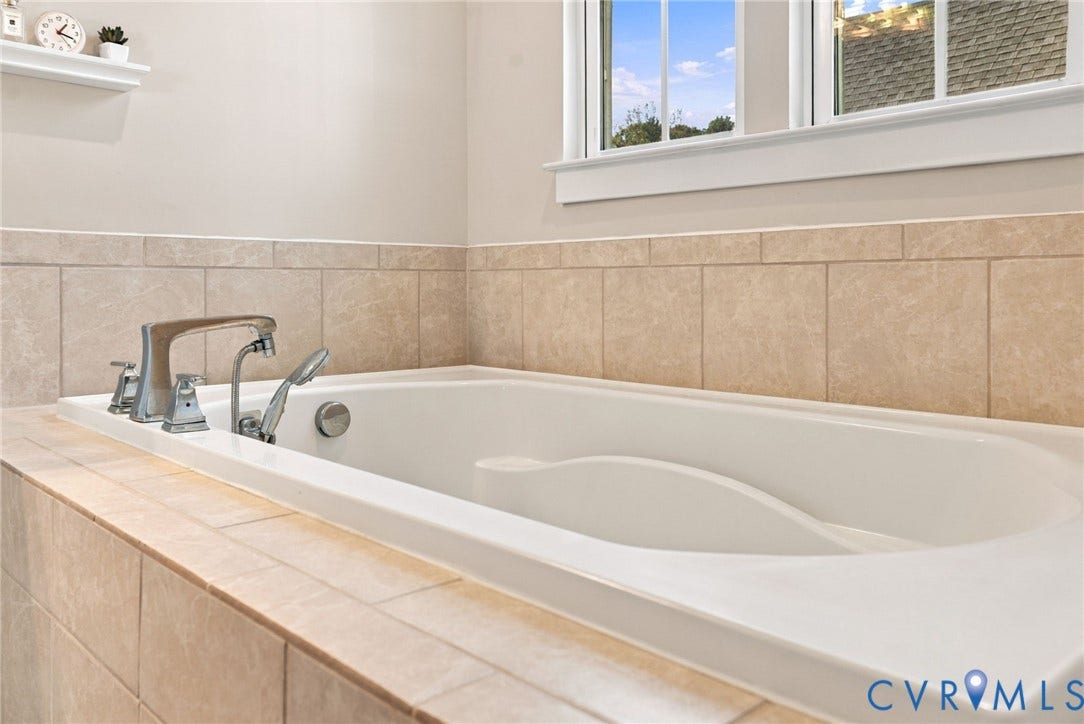 1716 German School Road, Westlake Heights, Richmond, VA 23225 Soaking tub featuring a tiled surround, deck-mounted chrome faucet with handheld shower attachment, and integrated wall-mounted shelving