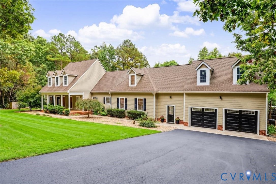 6650 Vintage Rose Lane, New Kent, VA 23140 Two-story exterior featuring tan siding, a multi-gabled roofline, dormer windows, an attached two-car garage with black doors, and a paved driveway