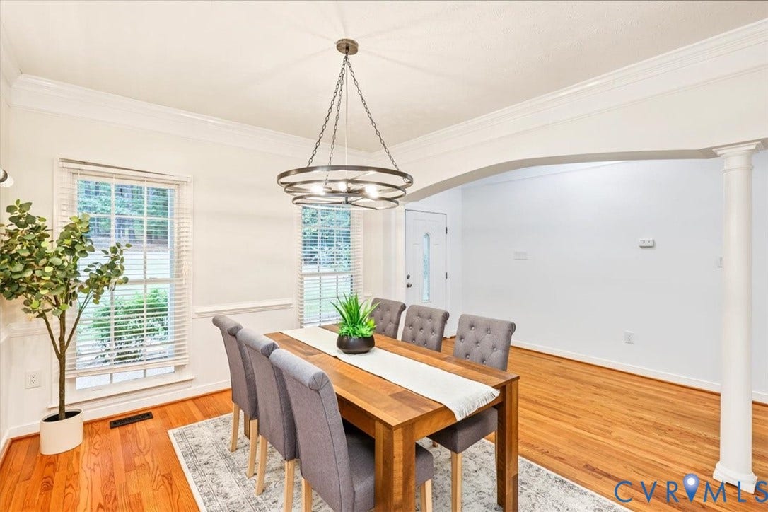 6650 Vintage Rose Lane, New Kent, VA 23140 Dining area featuring wood-finish flooring, crown molding, a circular tiered chandelier, a structural arched opening supported by a column, and white wainscoting