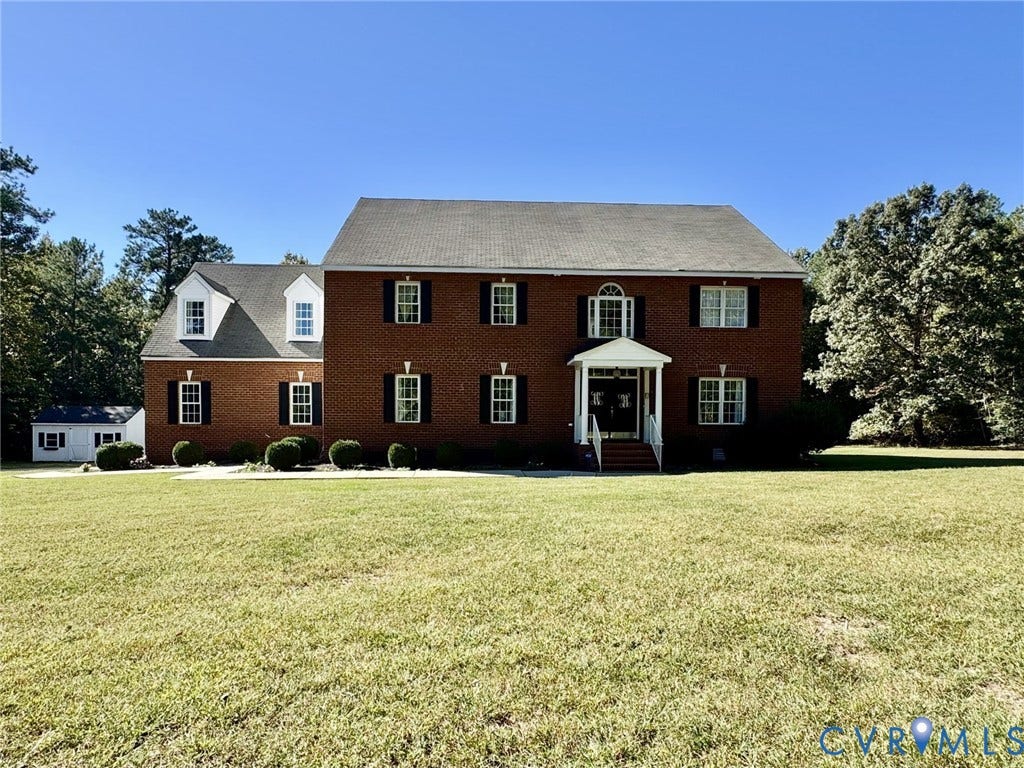 Two-story brick exterior featuring a covered front entryway, symmetrical window placement with shutters, dual dormer windows, and a paved walkway