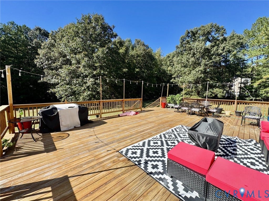 Expansive wood deck featuring a tiered structure, vertical wooden balusters, and a built-in cable lighting system, backed by a perimeter of mature trees