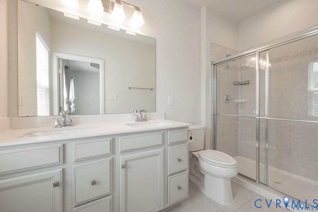 10221 Wenden Way, Hanover, VA 23005 Bathroom featuring a dual-sink vanity with light-toned cabinetry, solid-surface countertops, a full-width mirror, and a glass-enclosed shower with tile surround