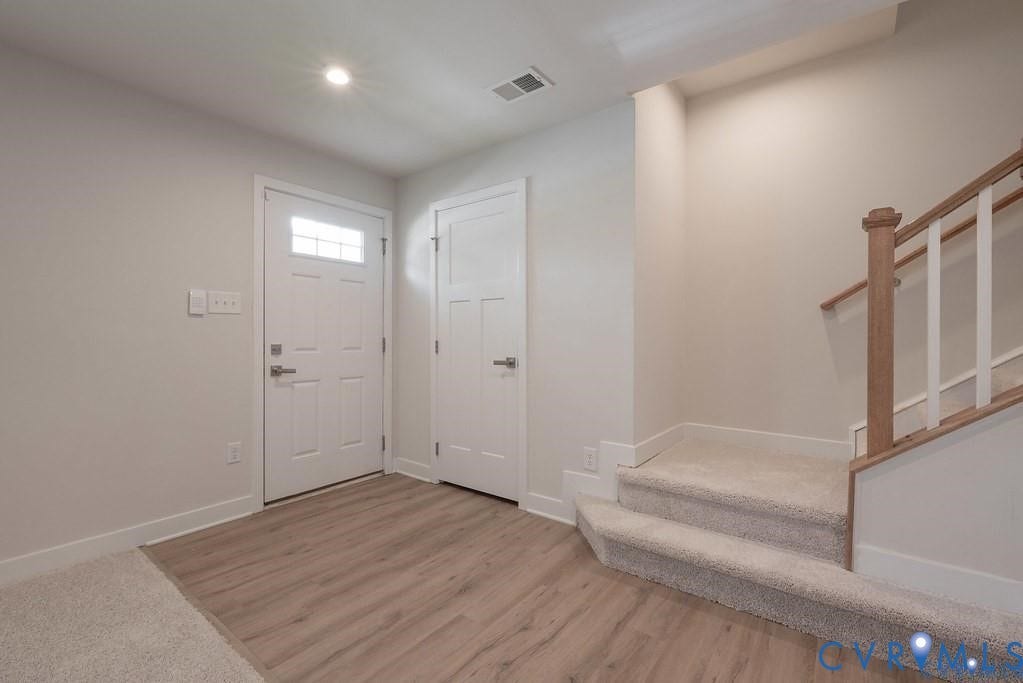10221 Wenden Way, Hanover, VA 23005 Entryway featuring a white paneled exterior door with a glass inlay, wood-finish flooring, and a staircase with a stained wood handrail and white balusters