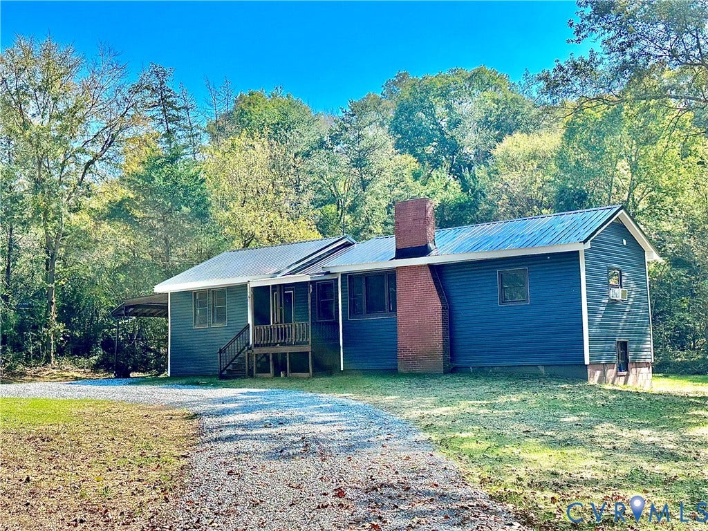 15051 BENT CREEK ROAD, Morven, Amelia, VA 23002 Exterior featuring dark blue horizontal siding, a standing-seam metal roof, a prominent exterior brick chimney, a covered porch, and a gravel driveway