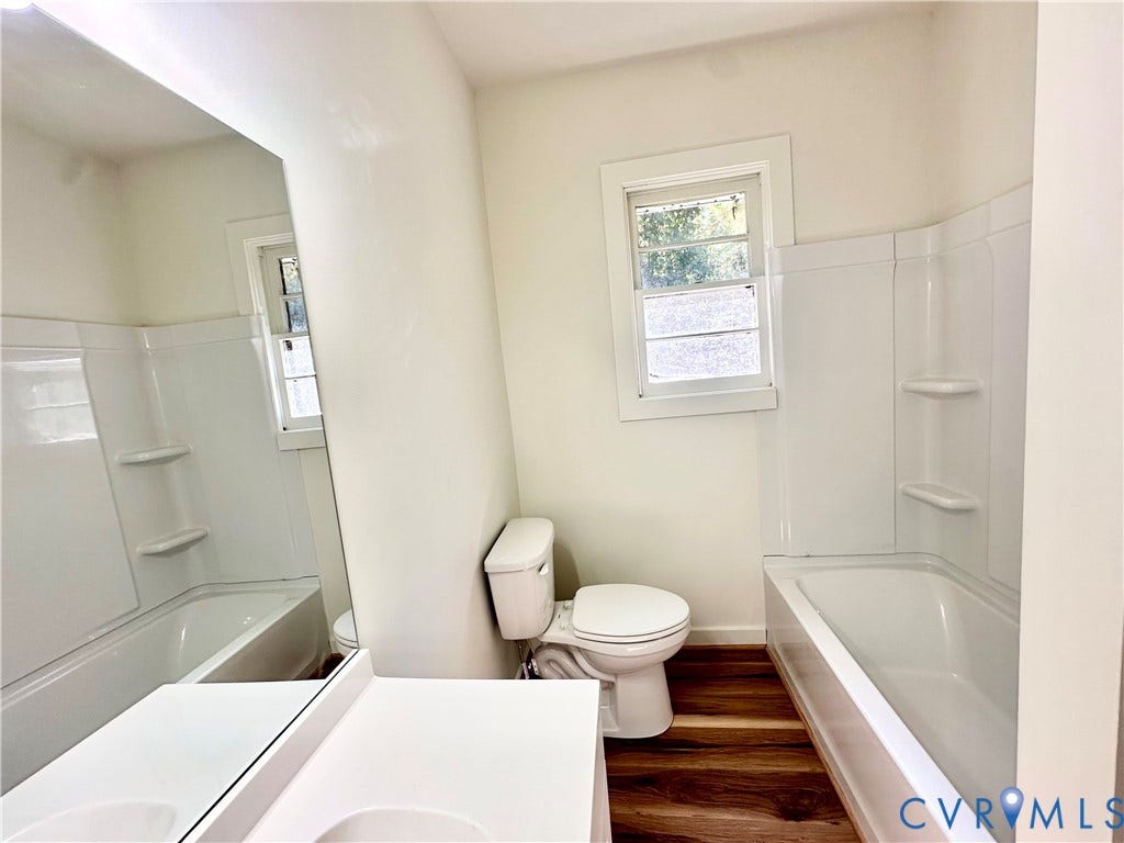 15051 BENT CREEK ROAD, Morven, Amelia, VA 23002 Bathroom featuring wood-finish flooring, a white vanity with a single basin, a large wall-mounted mirror, a tub-shower combination with integrated shelving, and a double-hung window