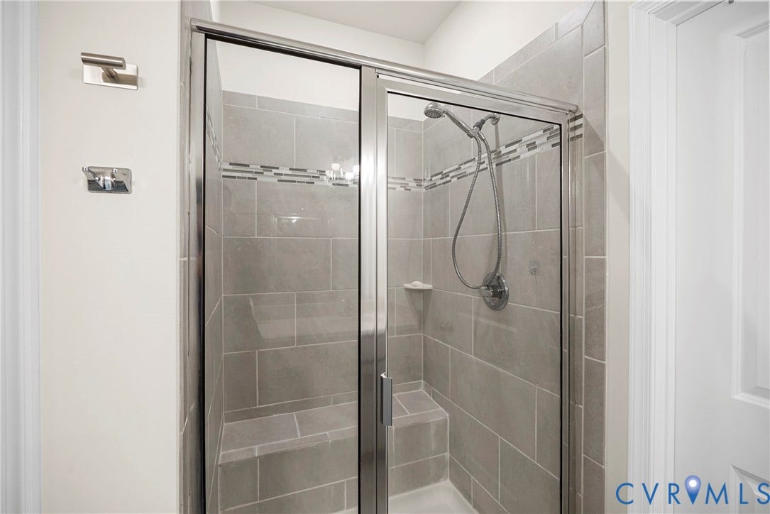 14501 Hancock Towns Drive, Chesterfield, VA 23832 Walk-in shower featuring large-format gray tile surround, decorative mosaic glass tile inlay, integrated corner bench seat, polished chrome hand-held shower fixture, and a framed glass door
