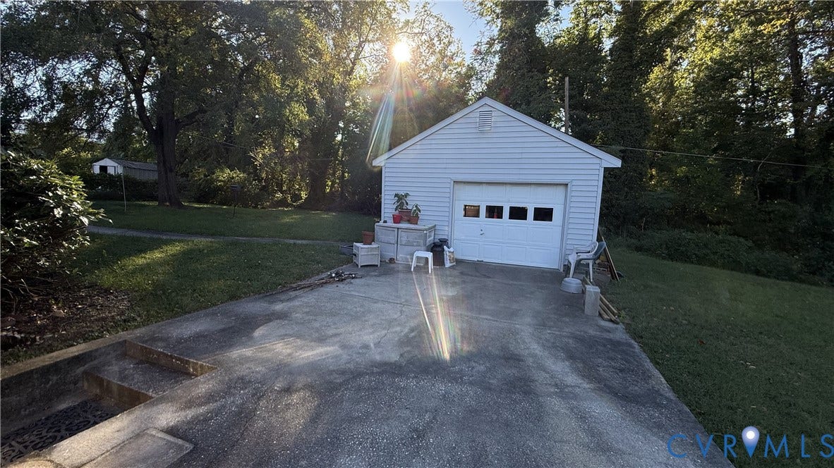 Detached garage with horizontal siding, multi-pane window garage door, concrete driveway, and expansive lawn