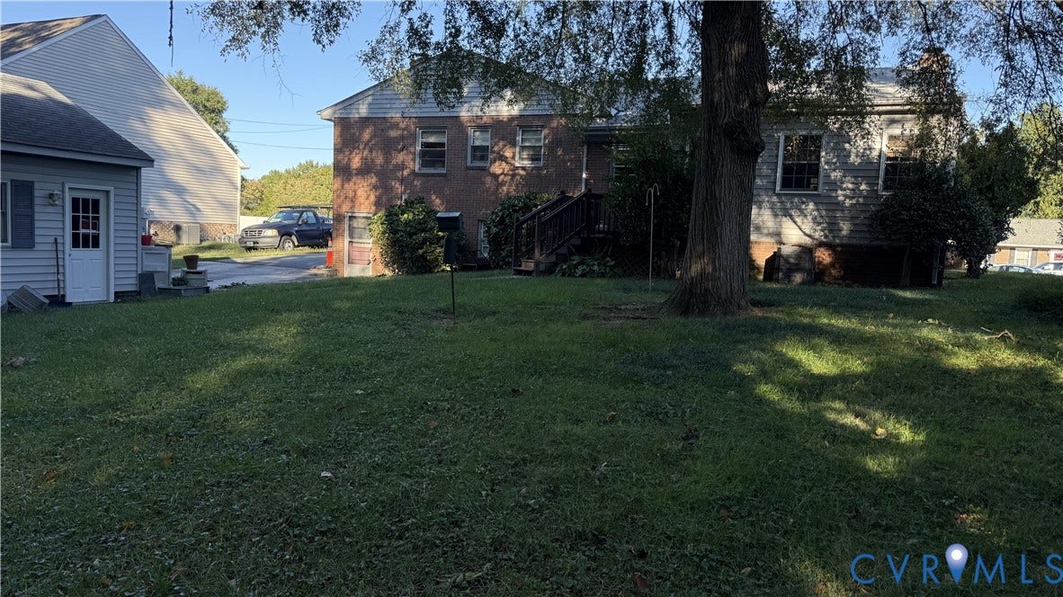 Brick and vinyl exterior featuring a spacious lawn, mature trees, and wooden staircase