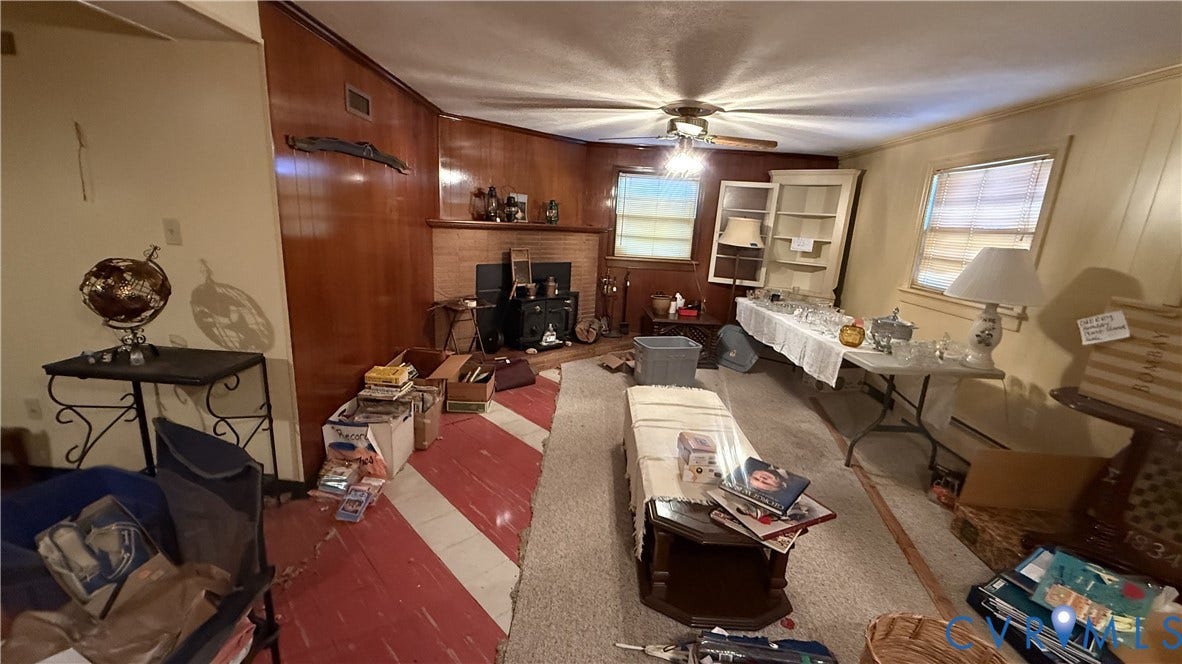 Wood-panelled accent wall, stone-surround fireplace, built-in shelving unit, and ceiling fan