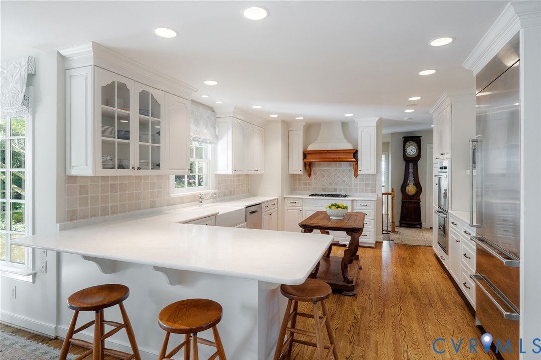 205 Poplar Lane, South Of Cary Street Rd, Richmond, VA 23226 The kitchen has white cabinetry with glass-panel accents, solid-surface counters, a farmhouse-style apron sink, recessed lighting, and gleaming hardwood floors.