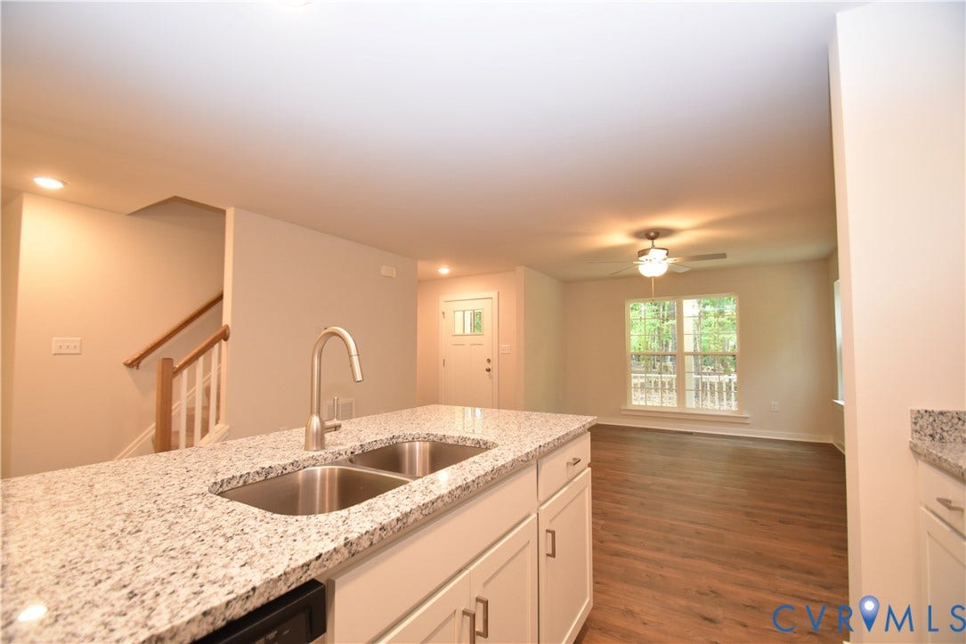 Lot 1 Bannister Town Road, Courtney Farms, Louisa, VA 23093 Kitchen island featuring a high-contrast stone countertop, double-basin stainless steel sink, and gooseneck faucet, paired with wood-finish flooring and staircase with wooden handrail