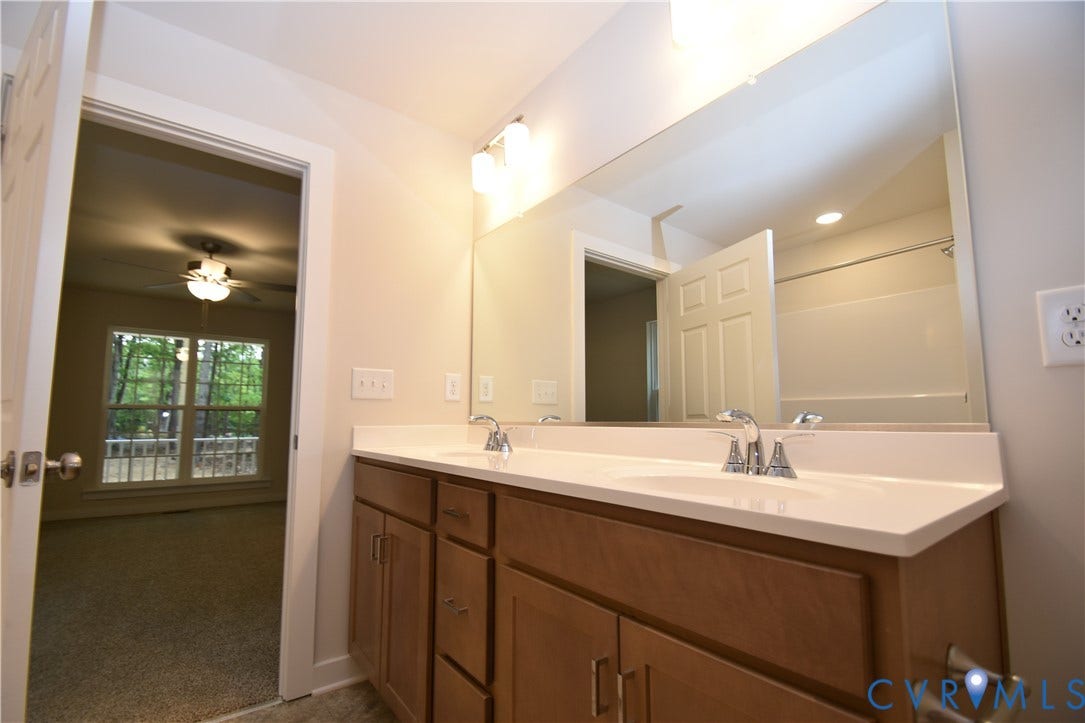 Lot 1 Bannister Town Road, Courtney Farms, Louisa, VA 23093 Dual-sink vanity featuring a light-toned solid surface countertop, wood-finish cabinetry, and a full-width wall mirror with integrated vanity lighting
