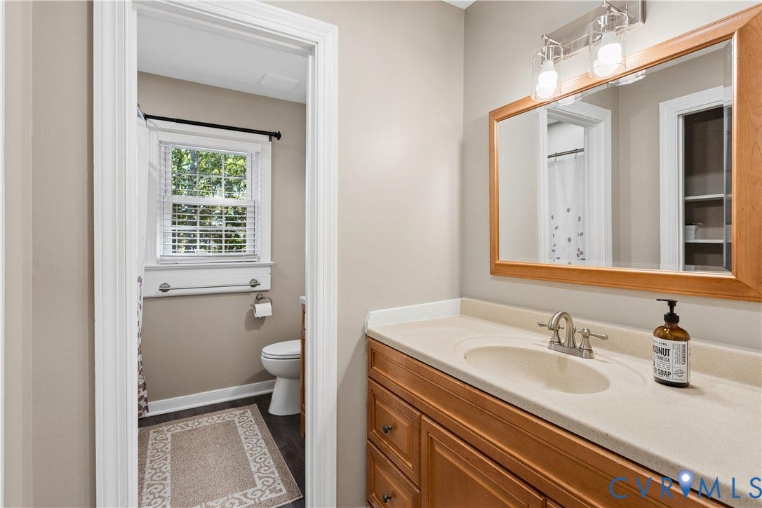 327 Huddersfield Drive, Chesterfield, VA 23236 Bathroom featuring a vanity with natural wood-tone cabinetry, solid surface countertop with integrated basin, three-light wall-mounted fixture, and a large wood-framed mirror