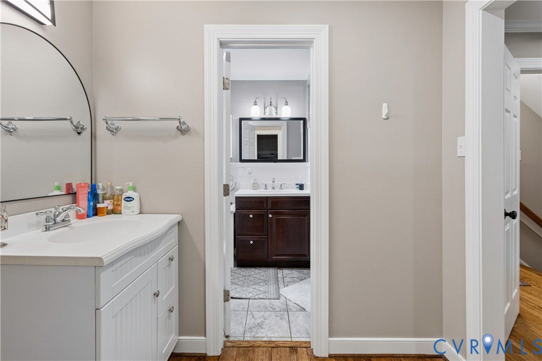327 Huddersfield Drive, Chesterfield, VA 23236 White vanity with a molded sink, polished chrome faucet, arched wall mirror, and secondary bathroom featuring a dark wood cabinet, multi-light fixture, and tiled flooring