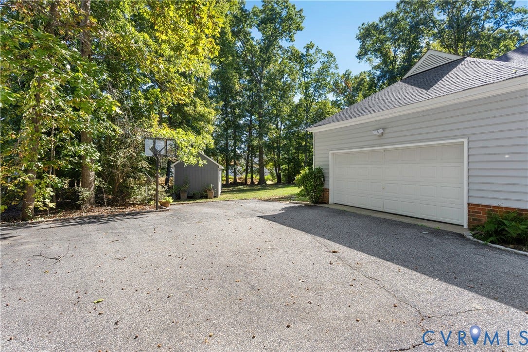 327 Huddersfield Drive, Chesterfield, VA 23236 Asphalt driveway featuring a multi-car garage, brick foundation detailing, attached basketball hoop, and a detached storage shed