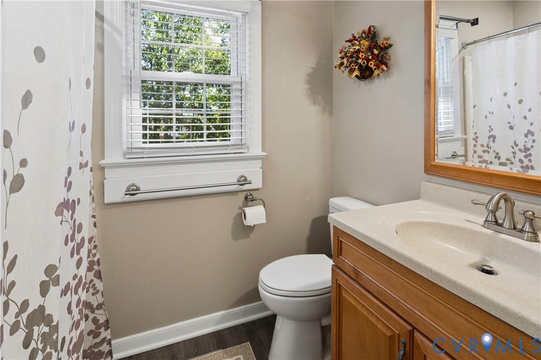 327 Huddersfield Drive, Chesterfield, VA 23236 Bathroom featuring a wood-toned vanity with an integrated solid surface countertop, dual-handle metal faucet, framed wall mirror, and a window with horizontal blinds